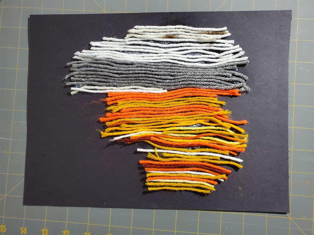 Gray white and orange yarn glued to a paper